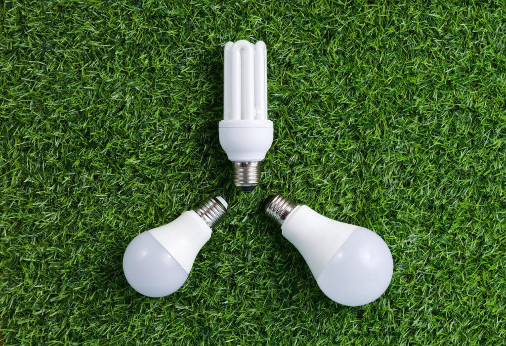 Three energy-efficient light bulbs placed on vibrant green grass, symbolizing sustainable energy.